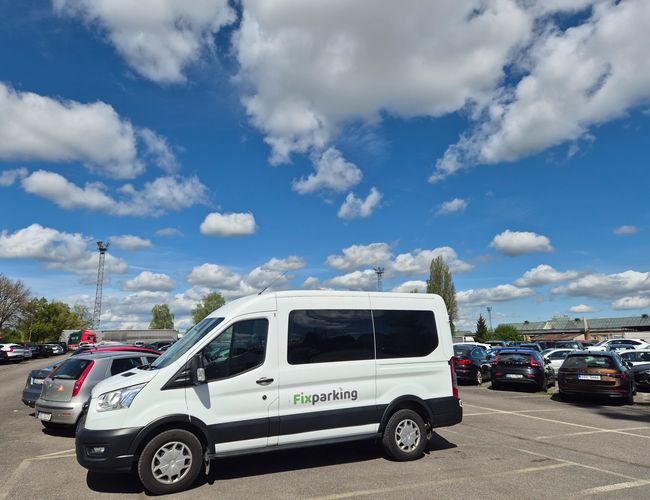 FixParking - Na parkingu stoi biały bus FixParking. Obok busa znajdują się zaparkowane samochody. Niebo jest błękitne z białymi chmurami.