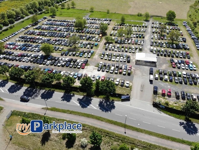Estacionamiento myParkplace - En el estacionamiento hay filas de coches. El área está abierta y sin techo. Se pueden ver árboles al fondo.