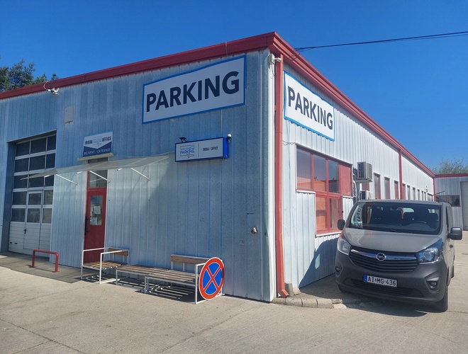 Parking BUDCAR - Widać zaparkowany bus przy budynku. Na budynku jest widoczny plakat reklamowy z nazwą parkingu.