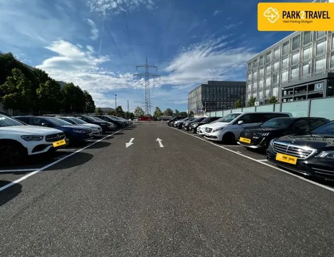 Parking Park2Travel Valet Outdoor – Parking jest przestronny i ogrodzony. Po obu stronach stoją zaparkowane samochody. Droga między nimi jest oznakowana.