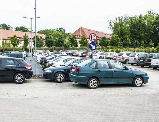 Parking Rondo - liczne samochody stoją w rzędach. Widać drogowskaz z ograniczeniem do 10 km/h. W tle zielone drzewa i budynki.