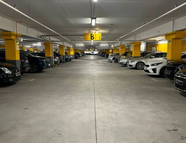 Parking MarcelinPark – Wewnątrz jest dużo miejsc parkingowych. Samochody stoją w równych rzędach. Teren jest jasno oświetlony.