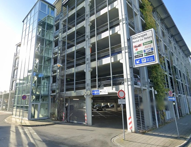 Widok na budynek parkingu Parkenplus z przeszkloną fasadą, oznakowaniem oraz wjazdem do wielopoziomowego parkingu.