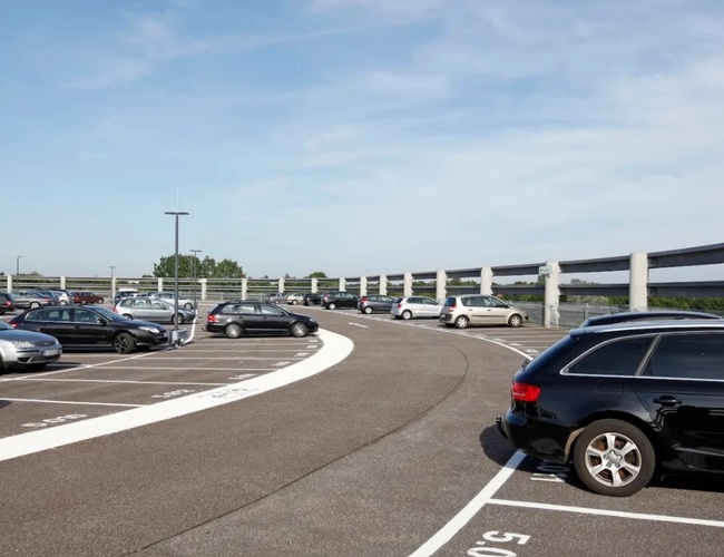 Otwarty parking P1 z wyznaczonymi miejscami postojowymi oraz szeroką drogą dojazdową w pobliżu terminalu lotniczego.