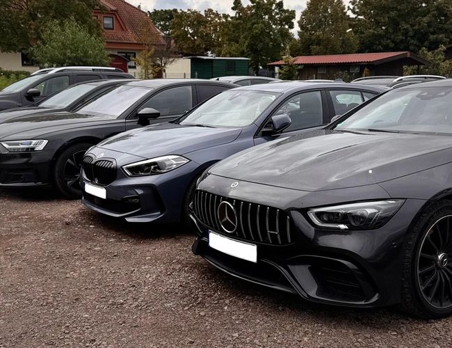 Prime Parking Valet – Cztery samochody stoją na żwirowym parkingu. Obok widać zielone otoczenie i budynki.