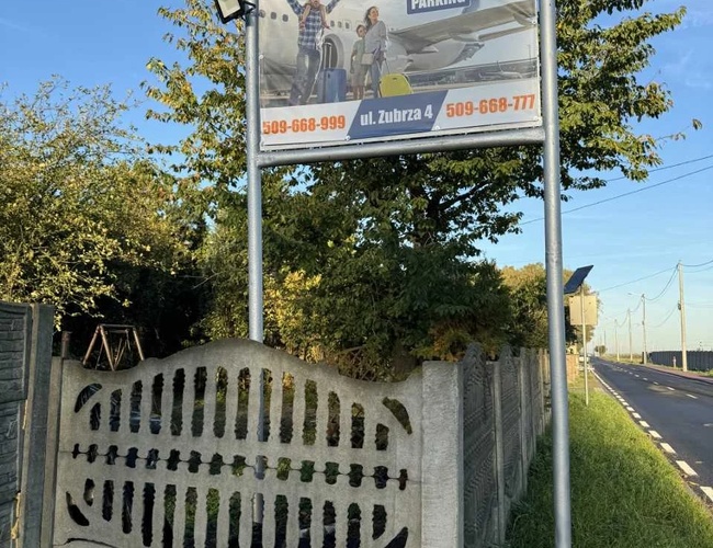 Estacionamiento Wings - Cartel publicitario junto a la carretera. Cerca de concreto. Árboles y cielo al fondo.
