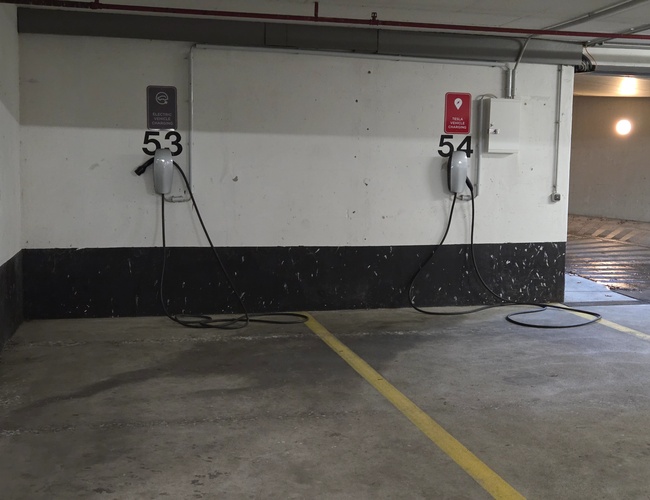 Atomis Hotel Munich Airport Parking Cubierto - Dos estaciones de carga para vehículos eléctricos número 53 y 54. Cada una tiene un cable conectado.