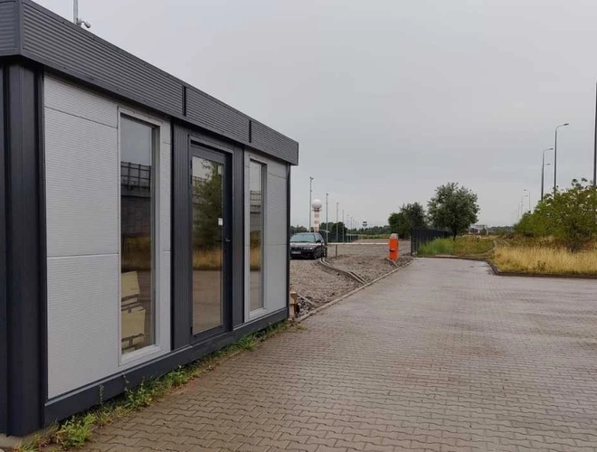 Easy Parking Express – En la foto se puede ver un pequeño edificio al lado del aparcamiento. Junto a él hay un coche. El terreno está adoquinado.