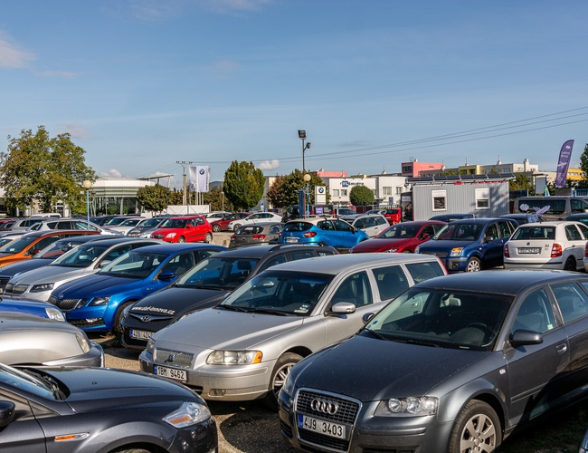 Parking Letim Brno - na parkingu stoi wiele samochodów. Teren jest otwarty i zadbany. W tle widoczne są drzewa i budynki.