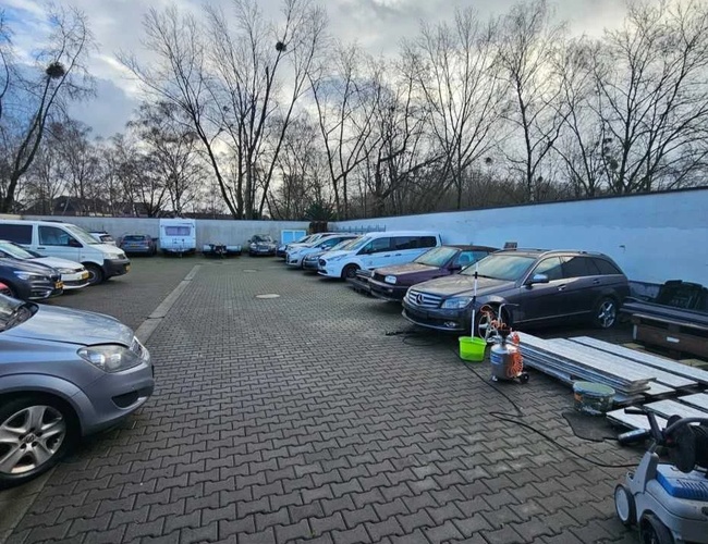 Parking Weltparking – Samochody zaparkowane są równolegle na kostce. W tle widać drzewa bez liści. Po prawej stronie leżą przedmioty.