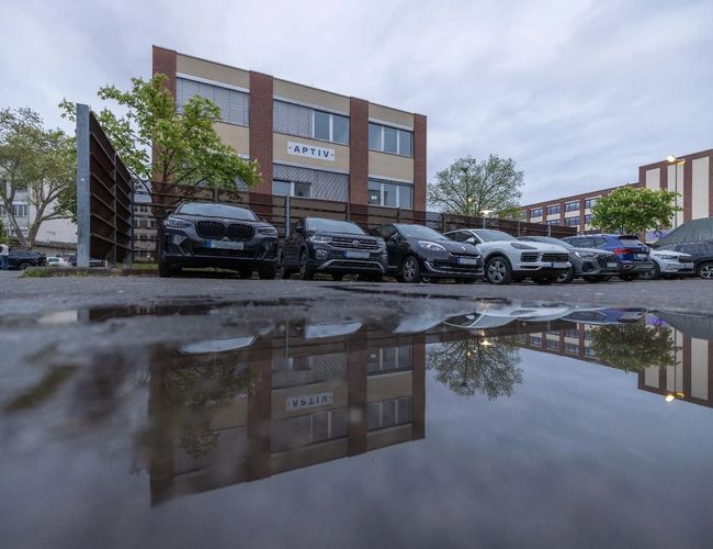 Parking Clean Valet Parkservice - Na parkingu stoją rzędy samochodów. Teren otoczony jest zielenią i budynkami.