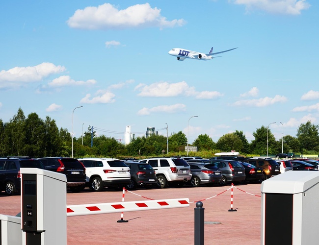 MEGA Parking - En el aparcamiento hay coches estacionados. En el fondo vuela un avión.