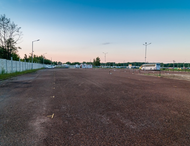 AAP-66 – Parking jest ogrodzony i oświetlony. Na placu stoją samochody. Teren jest pusty i przestronny.