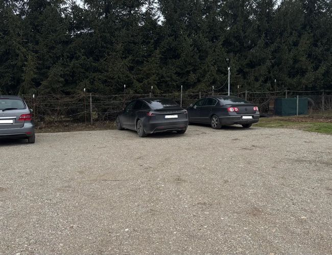 amochody zaparkowane na żwirowym, ogrodzonym parkingu Park4flight Maramureș, położonym w spokojnej okolicy z widoczną linią drzew w tle i szeroką przestrzenią manewrową dla pojazdów.