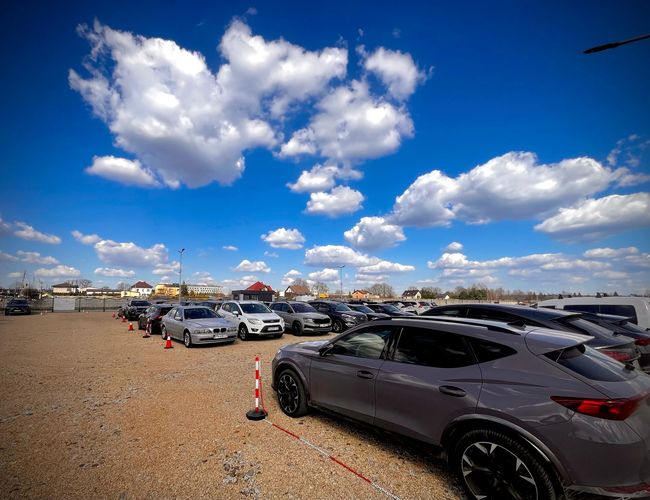 GoPark - Reihe geparkter Autos auf einem Kiesplatz. Der Parkplatz ist geöffnet, ohne Überdachung. Der Himmel ist mit weißen Wolken bedeckt.