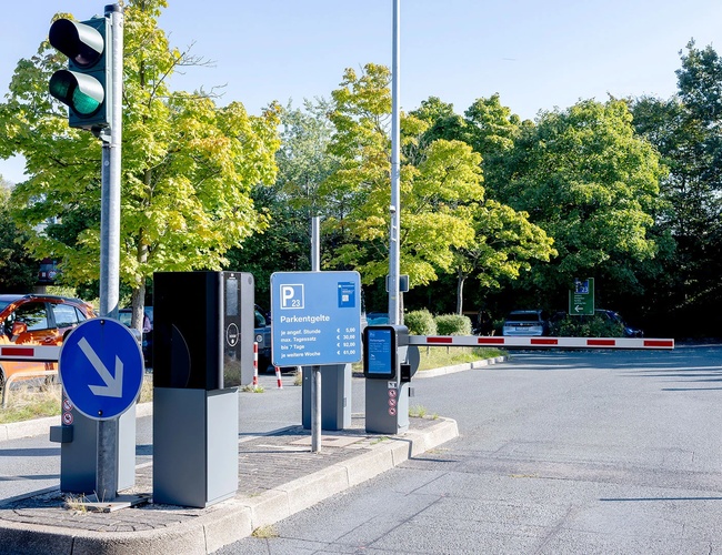 Wjazd na parking P23 z systemem szlabanów, oznakowaniem oraz drogą prowadzącą do strefy postojowej.