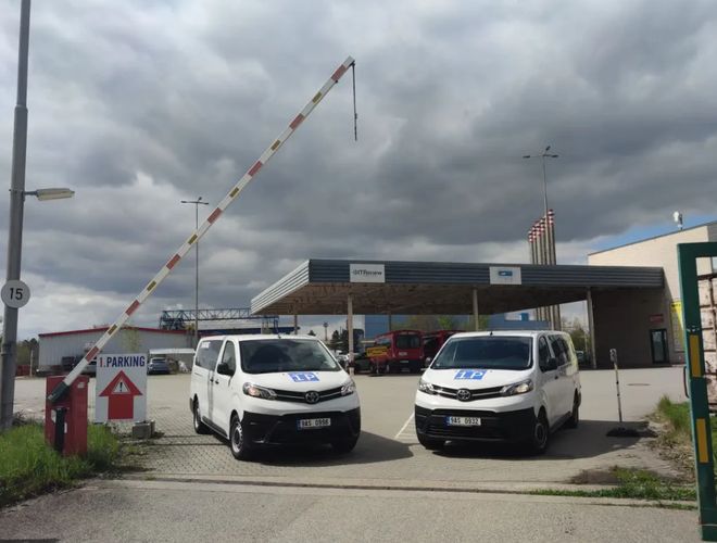 Wjazd na parking przy lotnisku w Pradze z szlabanem oraz busami transferowymi.