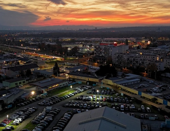 Parktiger Airport Parking 2 - estacionamiento lleno de coches al atardecer. El área está rodeada de edificios y calles iluminadas. En el horizonte se puede ver un cielo colorido.