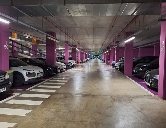Parking Low Valet - Podziemny parking z rzędami samochodów. Fioletowe filary oddzielają miejsca. Oświetlenie sufitowe zapewnia jasność.