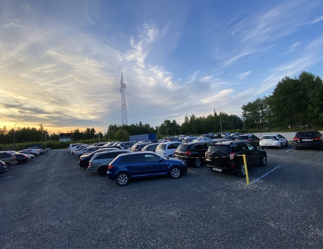 Odstupová Zóna - pri trase S7. Veľa zaparkovaných áut na štrkovom povrchu. Okolie zelene a energetický stĺp v pozadí.