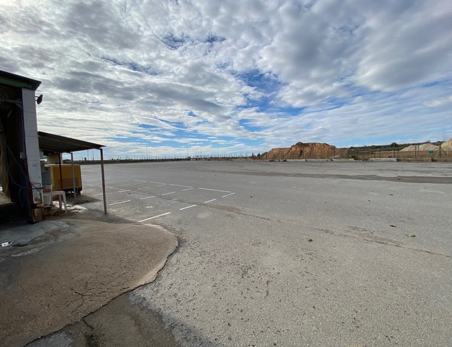 Parkovisko Odkryj-Auto - Rozsiahle asfaltové parkovisko s vyznačenými miestami. Na obzore je vidieť plot a zemné násypy.