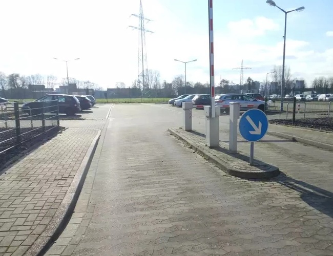 Parking Park&Fly Düsseldorf - Plac jest wybrukowany i oświetlony lampami. Widać szlaban i kilka zaparkowanych samochodów.
