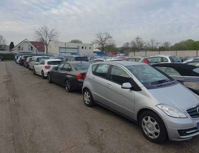 Parking Weltparking – na parkingu stoją zaparkowane samochody. Teren jest ogrodzony. W tle widoczny jest budynek.