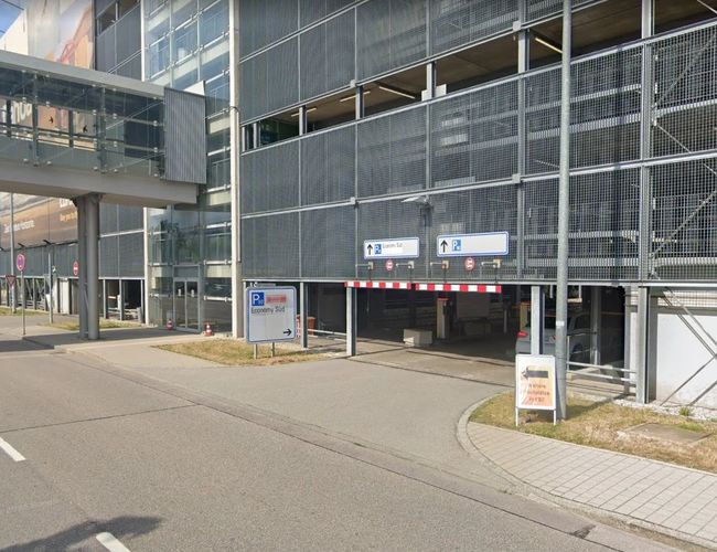 Wjazd do parkingu wielopoziomowego z oznakowaniem i szlabanem.