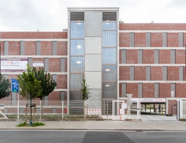 Parking Best Valet Park Service – budynek z cegły i betonu. Na pierwszym planie znajduje się ogrodzenie i brama wjazdowa.