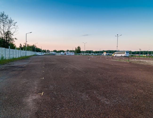 AAP-66 – Parking jest ogrodzony i oświetlony. Na placu stoją samochody. Teren jest pusty i przestronny.