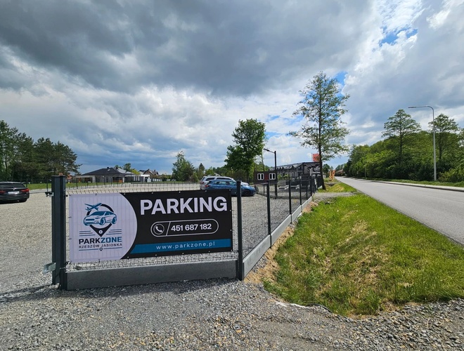ParkZone - Estacionamiento cercado con publicidad visible. Al lado pasa una carretera. Hay varios coches en el área.