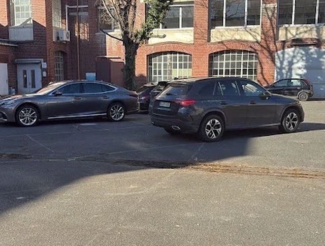 Parkoló Parkfinder24 Valet - személygépkocsi számára parkoló. Fel- és munkált terület, nem kerített, a téglából épült épület előtt. Látható pár jármű.