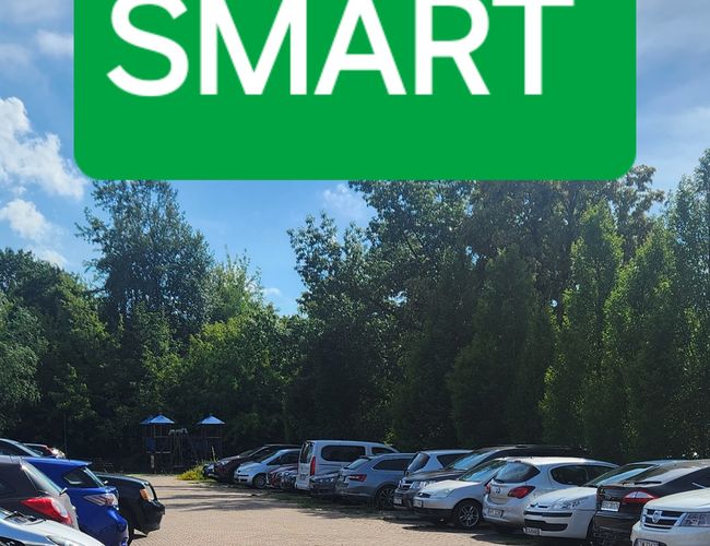 Aparcamiento Barato y Seguro SMART - los coches están estacionados en una superficie adoquinada. Al fondo se ven árboles y un parque infantil.