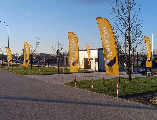 ParkON - På bildet ser du en parkeringsplass med gule flagg. Området er inngjerdet og opplyst med gatelys. Tilbaket står biler.