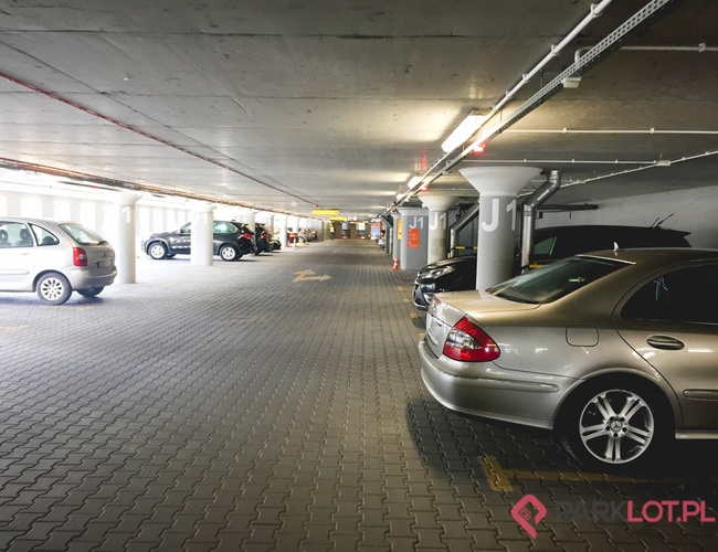 Oficiálne parkovisko Letiska P2 – podzemné parkovisko s viacerými miestami. Niekoľko zaparkovaných áut sa nachádza pri betónových stĺpoch. Svetlo je umelé, steny sú šedé.