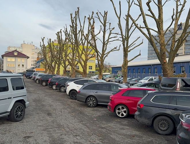Parkoló Park & Go Valet – kavicsos aljzatú parkolóhely. Körbezárva kerítéssel, látható parkoló autók. Körülötte épületek és fák.