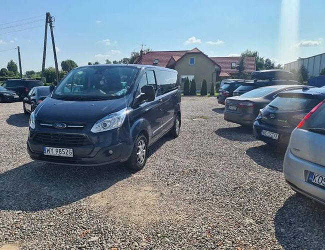 Parking Dominik – Żwirowa nawierzchnia, kilka zaparkowanych samochodów. W tle dom z czerwonym dachem.