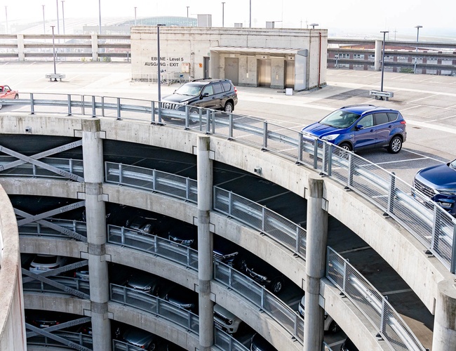 Spiralny wielopoziomowy parking P1 przy lotnisku z samochodami poruszającymi się po rampie prowadzącej na kolejne poziomy postojowe.