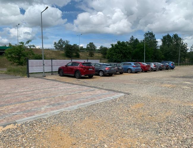 Victory Cars P2 – Parkovanie je čiastočne z dlažby a štrku. Automobily stoja v rade. Viditeľný je kovový plot.