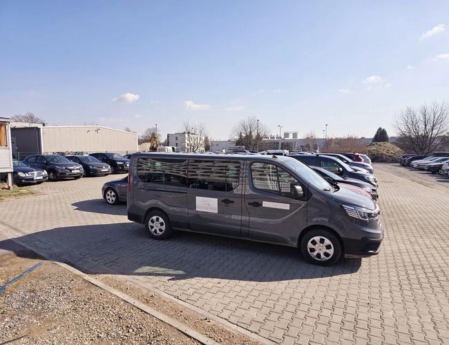Parking Olo Car Park - Pojazdy stoją na utwardzonym placu. Teren jest przestronny i częściowo ogrodzony. Jest słoneczny dzień.