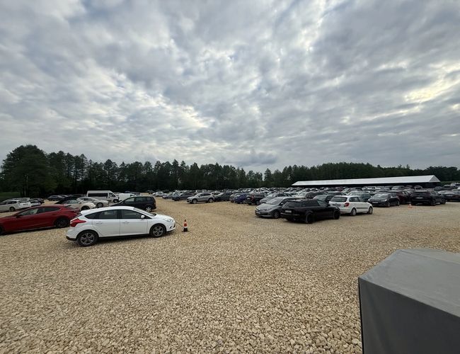 FlyParking – Duży parking żwirowy pełen samochodów. Teren otacza las.