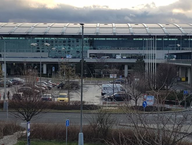 Parkovanie Smile Parking - parkovisko plné áut pred letiskom. V pozadí terminál s veľkými oknami. Vpredu cesta a dopravné značky.