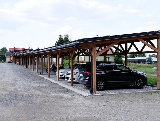 Parking Zielony Kompleks Dwór Ostoya – Zadaszony parking z kilkoma samochodami. Obok stoi motocykl. Teren jest utwardzony i przestronny.