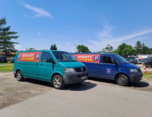 Parking Avanti - Dos coches con el logo de la empresa están uno al lado del otro. El fondo está formado por árboles y un cielo claro.