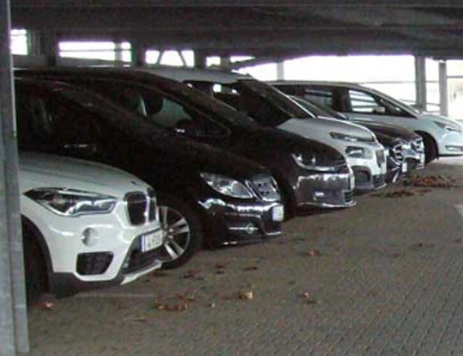 ParKing’s Düsseldorf Covered Valet – szereg zaparkowanych samochodów pod zadaszeniem. Teren jest wyłożony kostką brukową. Widać też metalowe filary.