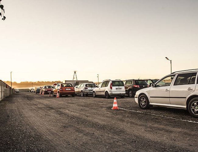 PERI Parking - Estacionamiento con cercado y mantenido en estilo gravilloso. Coches aparcados en paralelo junto a un muro de concreto.