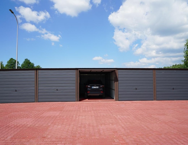 VIP Garáže MEGA Parkovisko - Šedá garáž s otvorenými dverami. Uvnitř stojí auto. Modrá obloha nad garážou.