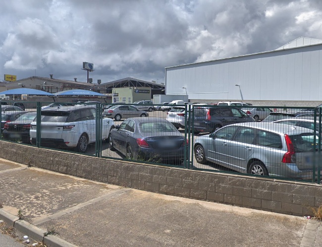Estacionamiento Park and Greet Valet - en la imagen se puede ver un estacionamiento cercado con coches estacionados. Al fondo hay edificios industriales.
