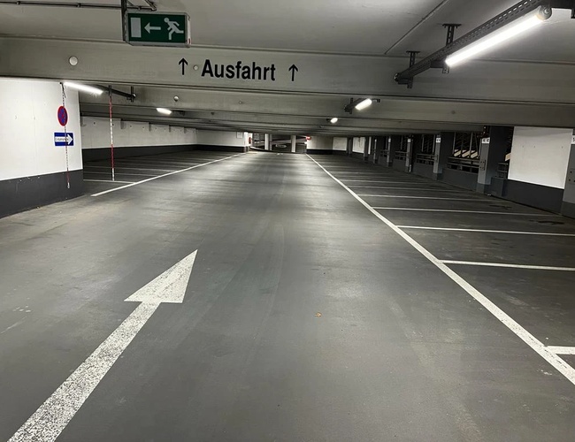 Parkovisko Park2Travel Valet Garage - Prázdna parkovacia hala s jasnou značkou. Na strope sú lampy. Na podlahe je vidieť smerovú šípku.