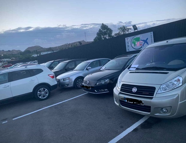 PARK SANSECAR VALET - Parking jest pełen aut. W tle widoczna tablica z logo. Teren jest ogrodzony i przestronny.